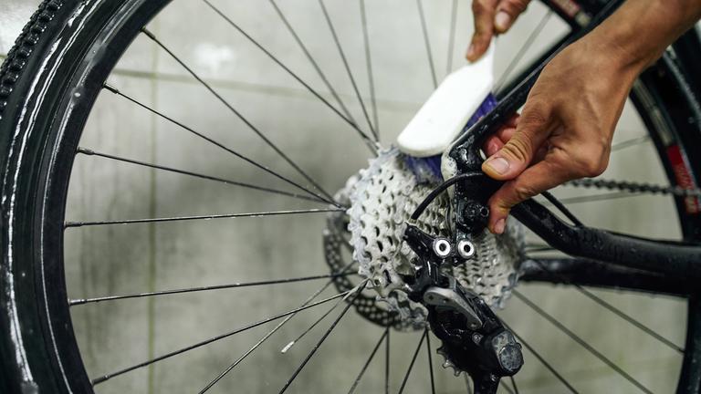 Ein Mann putzt die Speichen eines Fahrrades mit einer Bürste.