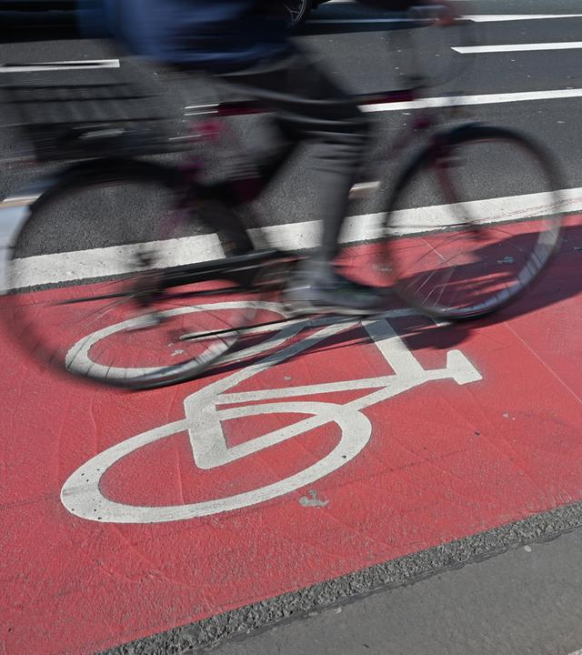 Ein Fahrradfahrer fährt auf einem rot abgegrenzten Radweg mit Fahrrad-Piktogramm.