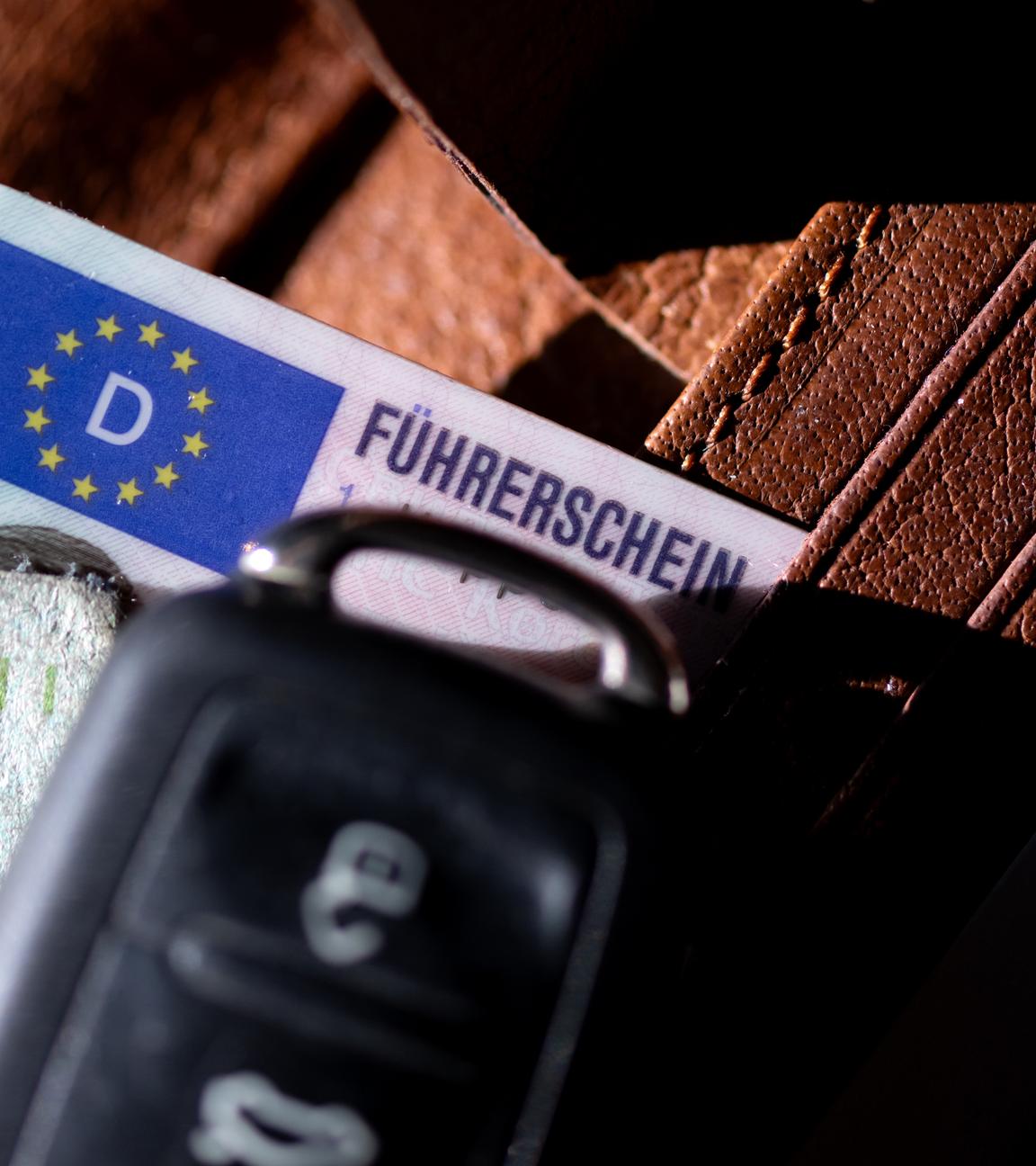 Ein Führerschein, ein Autoschlüssel und eine Zulassungsbescheinigung liegen auf einem Portemonnaie. 