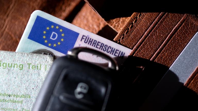 Ein Führerschein, ein Autoschlüssel und eine Zulassungsbescheinigung liegen auf einem Portemonnaie. 