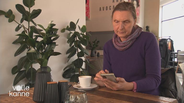 Frau sitzt am Tisch und schaut auf ihr Smartphone.