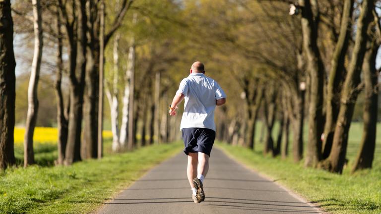 Ein Mann joggt auf einer Landstraße.