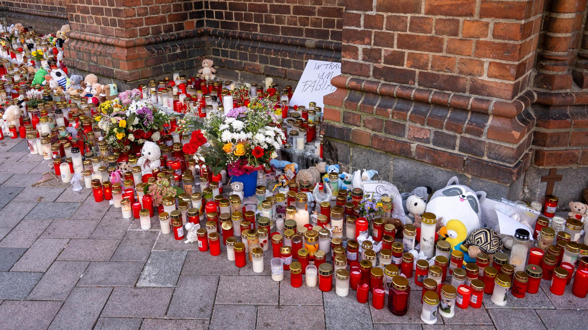 Vor der Marienkirche stehen Grablichter, Blumen und Plüschtiere im Gedenken an den vermissten achtjährigen Fabian, auf einem Schild steht "In Trauer um Fabian". 
