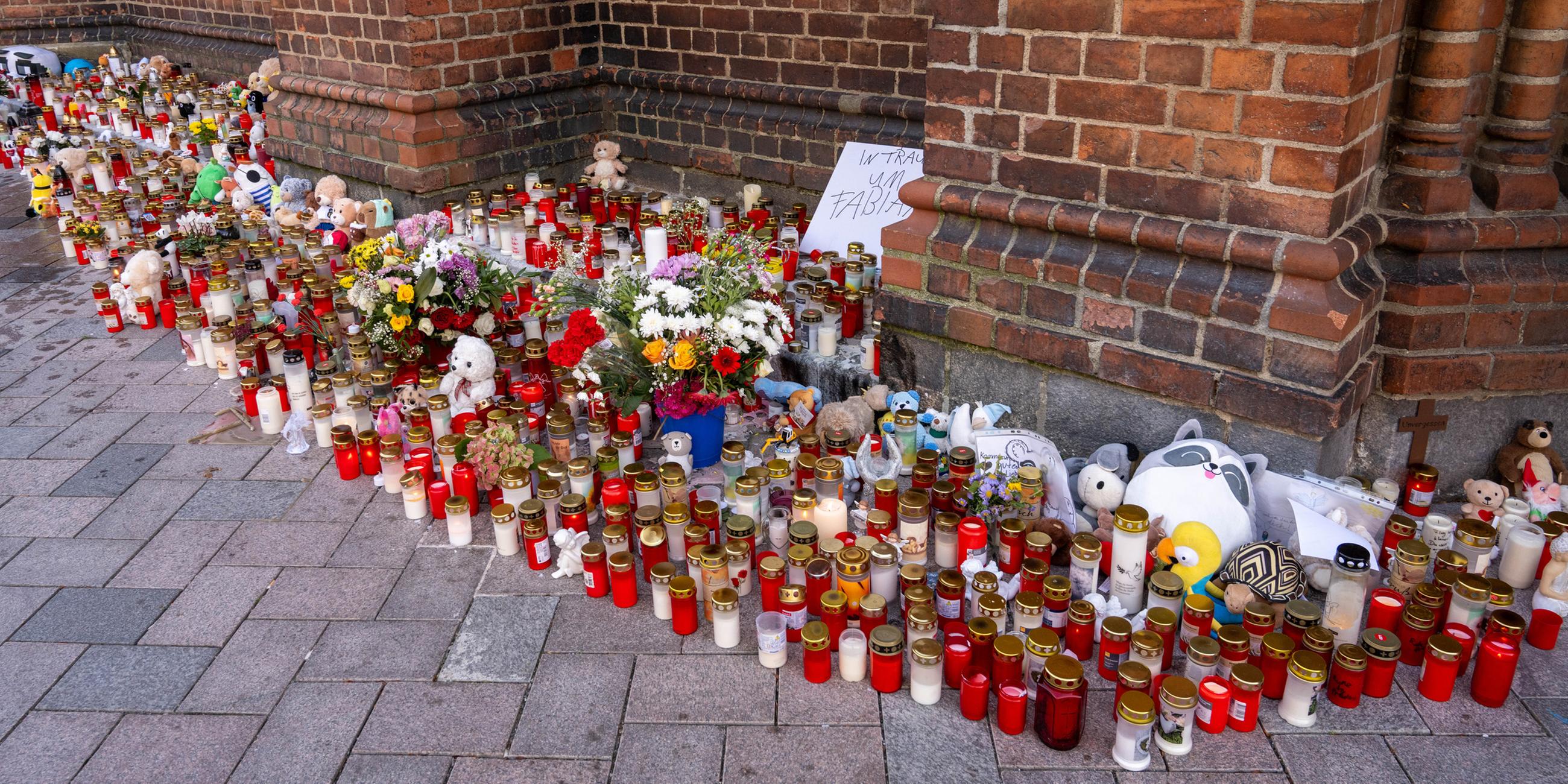 Vor der Marienkirche stehen Grablichter, Blumen und Plüschtiere im Gedenken an den vermissten achtjährigen Fabian, auf einem Schild steht "In Trauer um Fabian". 