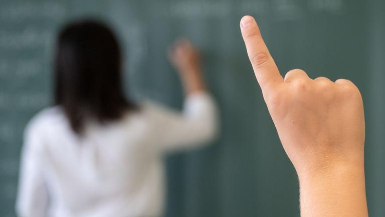 08.07.2020, Baden-Württemberg, Marbach am Neckar: Ein Schüler meldet sich während einer Unterrichtsstunde einer fünften Klasse des Friedrich-Schiller Gymnasiums, während die Lehrerin an die Tafel schreibt. 