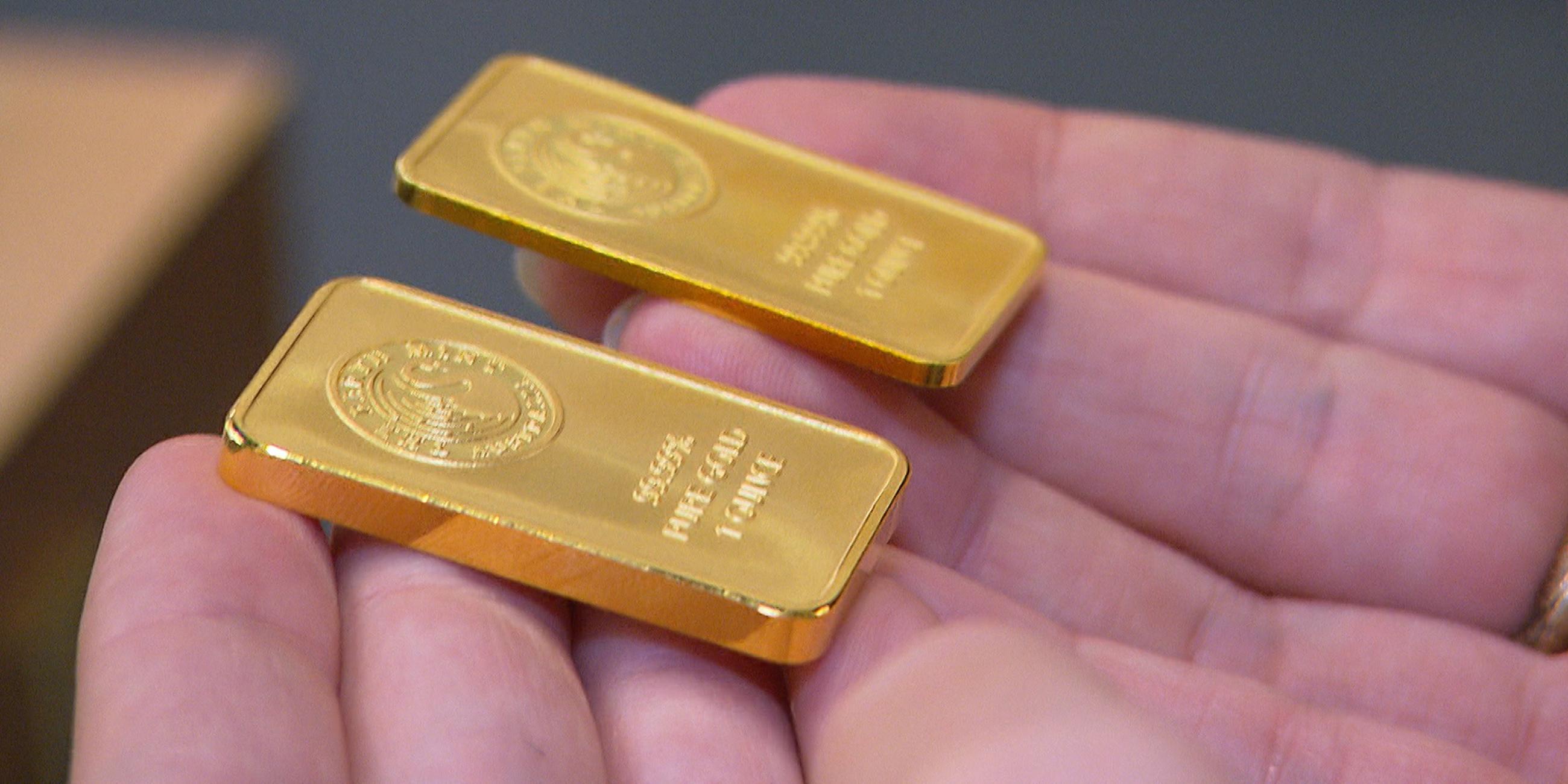 "Falsche Versprechen - So lassen wir uns manipulieren": Nahaufnahme von zwei kleinen Goldbarren, die auf den Fingern einer Person liegen.