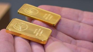 "Falsche Versprechen - So lassen wir uns manipulieren": Nahaufnahme von zwei kleinen Goldbarren, die auf den Fingern einer Person liegen.