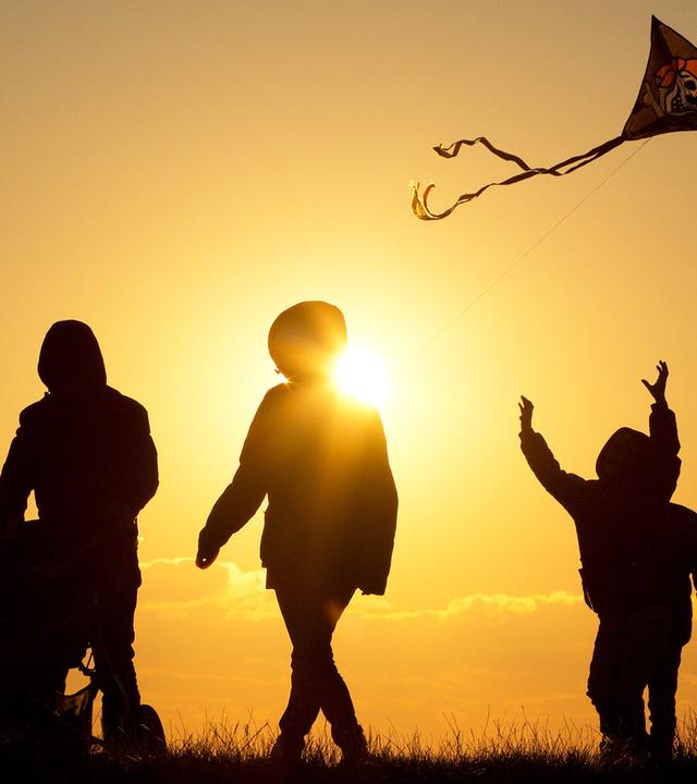 Familie geht bei Sonnenuntergang mit Kinderwagen und Drachen spazieren 