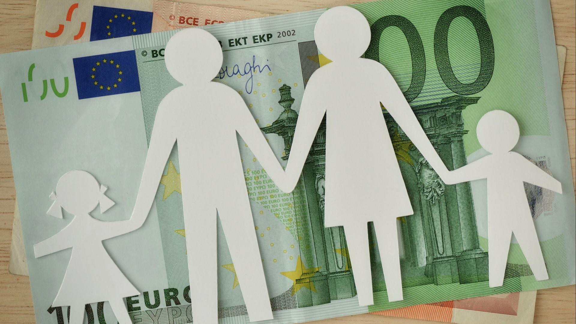 Eine Familie im Scherenschnitt liegt über einem 100-Euro-Schein.