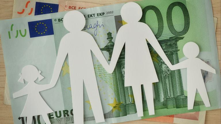 Eine Familie im Scherenschnitt liegt über einem 100-Euro-Schein.