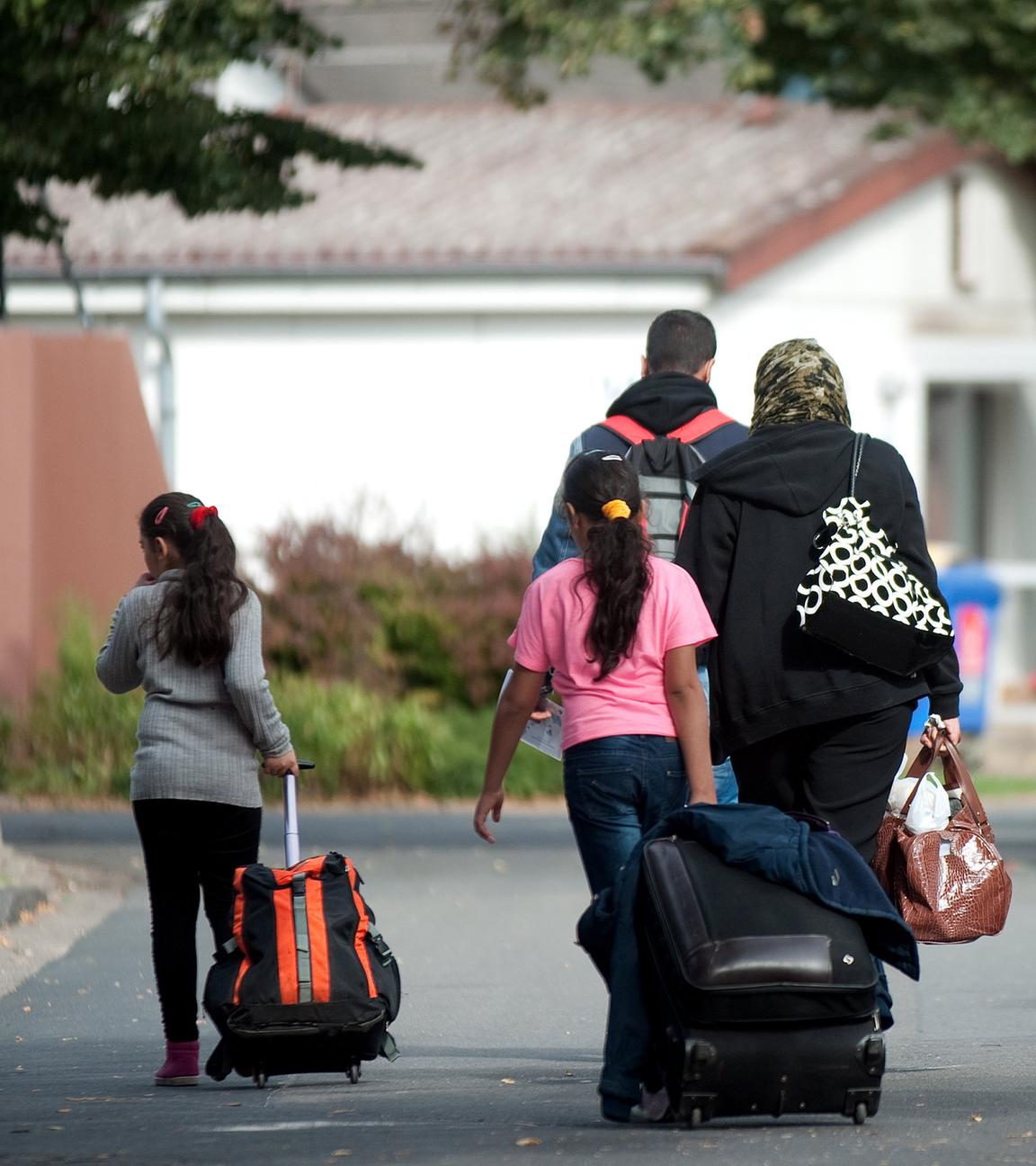 Flüchtlinge mit Koffern und Plastiktüten gehen im Grenzdurchgangslager Friedland an Unterkünften vorbei.