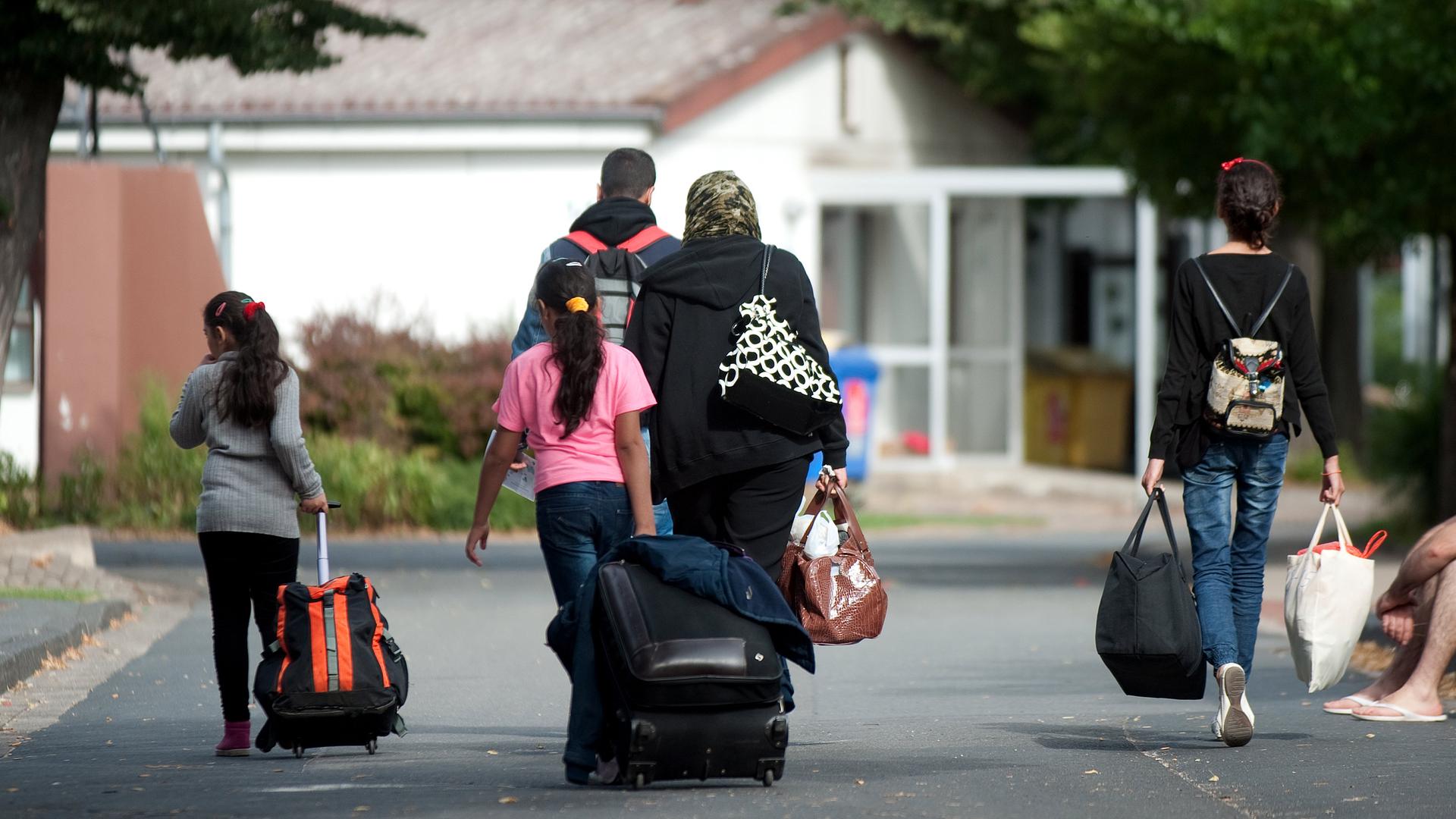 Flüchtlinge mit Koffern und Plastiktüten gehen im Grenzdurchgangslager Friedland an Unterkünften vorbei.