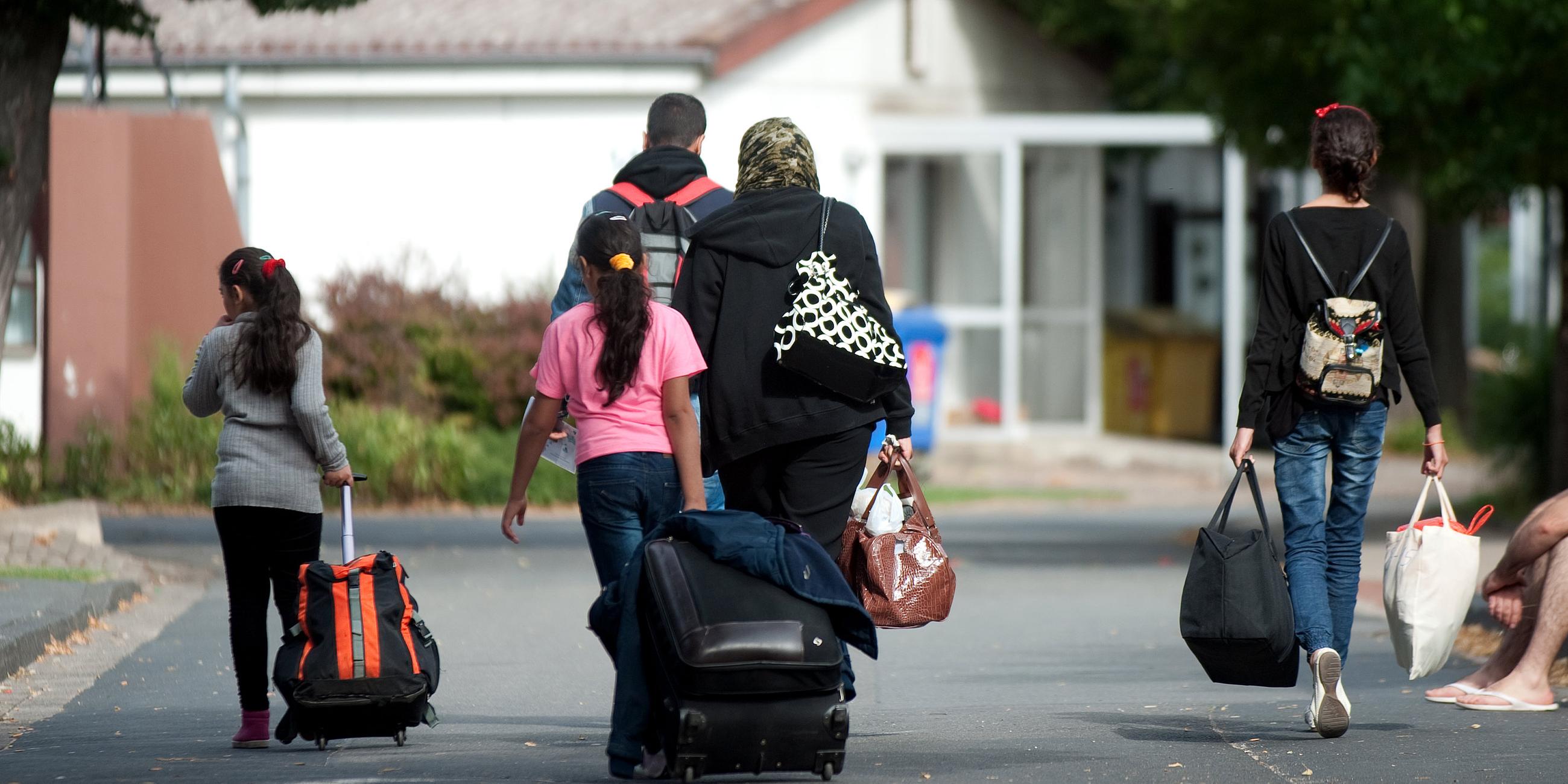 Flüchtlinge mit Koffern und Plastiktüten gehen im Grenzdurchgangslager Friedland an Unterkünften vorbei.