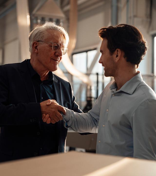 Ein älterer Geschäftsmann schüttelt einem jüngeren Mitarbeiter die Hand.