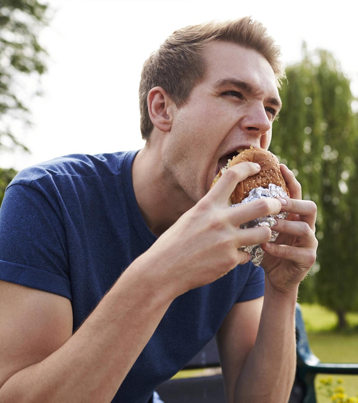 Ein junger Mann isst eine Hamburger in einem Park