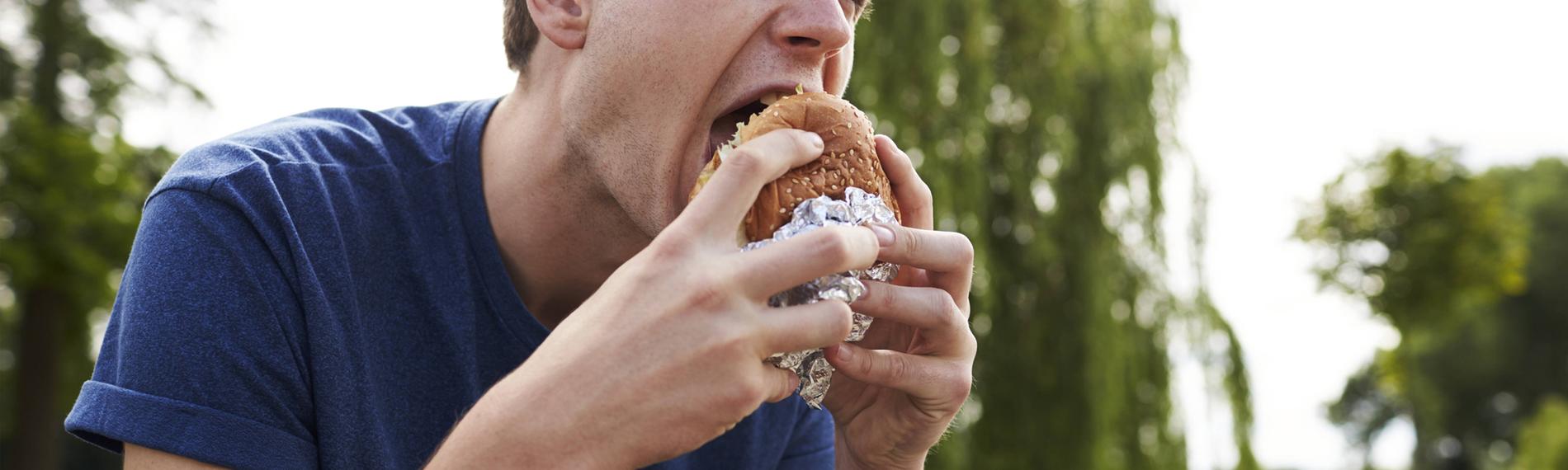 Ein junger Mann isst eine Hamburger in einem Park