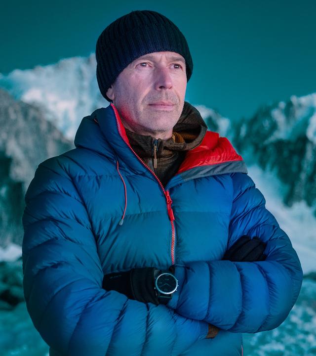 Dirk Steffens steht im Abendlicht auf dem Mont Blanc Massiv vor einem von innen heraus erleuchteten Zelt.