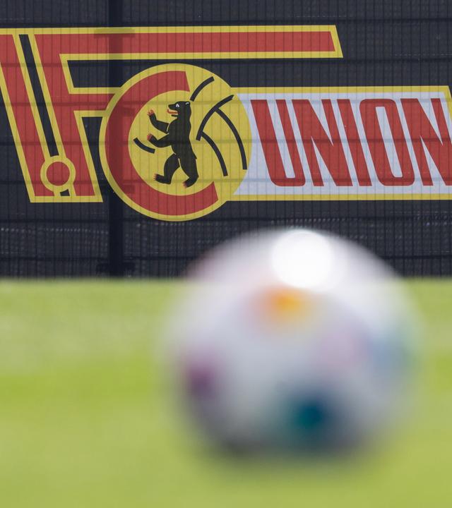 Ein Fußball liegt auf dem Rasen. Im Hintergrund ist das Logo vom 1. FC Eisern Union zu sehen.