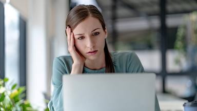 Junge Frau, die am Arbeitsplatz auf ihren Laptop schaut