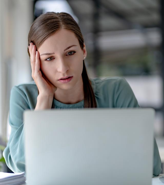 Junge Frau, die am Arbeitsplatz auf ihren Laptop schaut