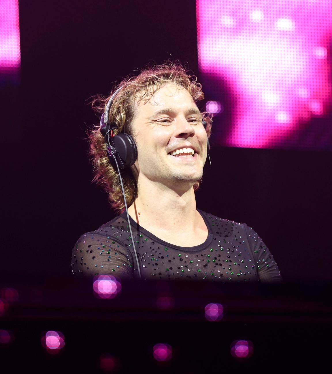 Felix Jaehn steht während seines Live-Auftritt beim Rainbow Festival am DJ-Pult. Um ihn herum sind pinke Lichtprojektionen.