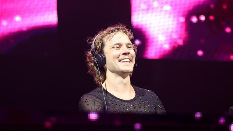 Felix Jaehn steht während seines Live-Auftritt beim Rainbow Festival am DJ-Pult. Um ihn herum sind pinke Lichtprojektionen.