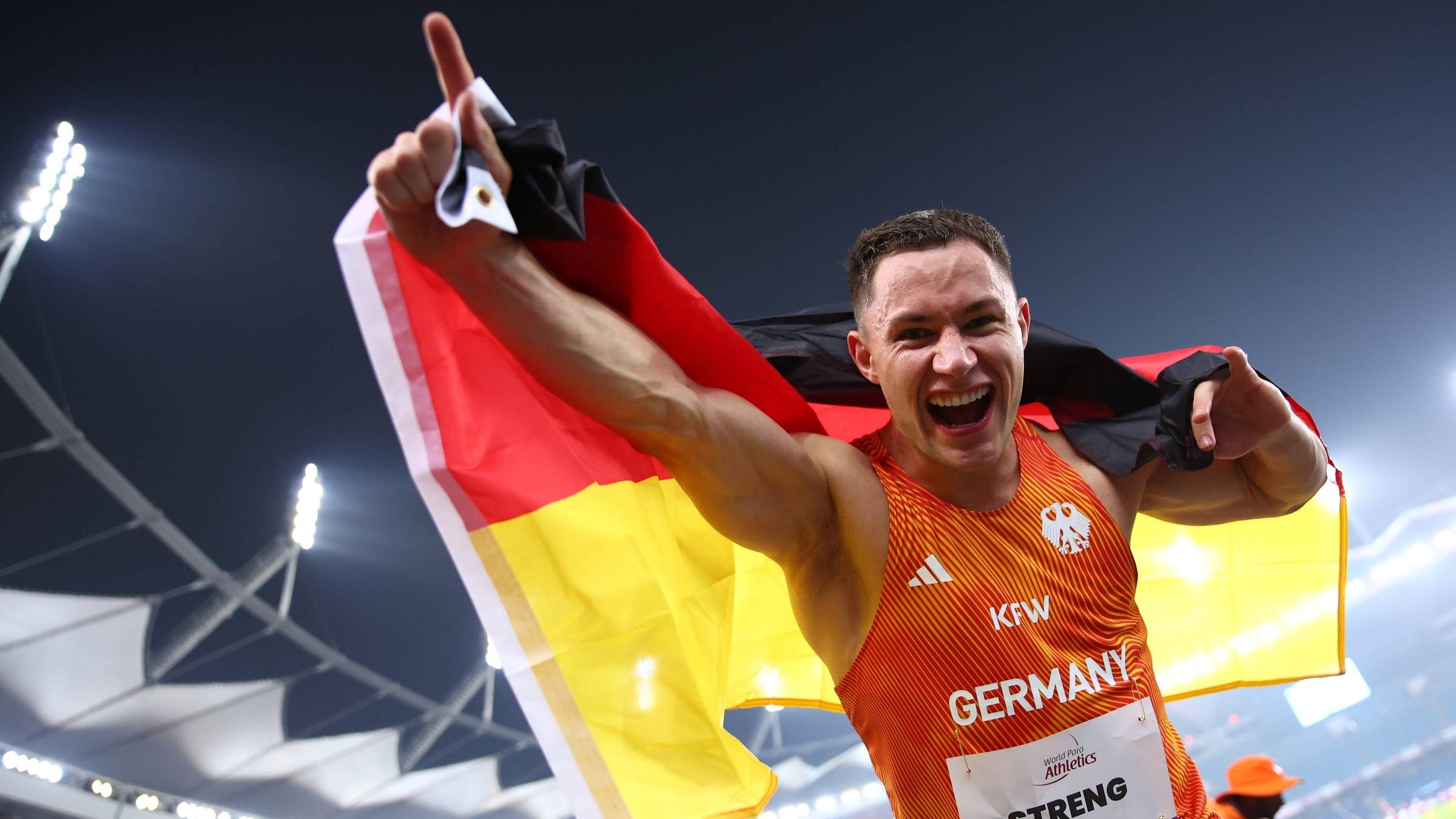 Felix Streng von Team Deutschland jubelt mit der Deutschland-Fahne auf dem Rücken über Gold im 100-Meter-Finale der Klasse T64