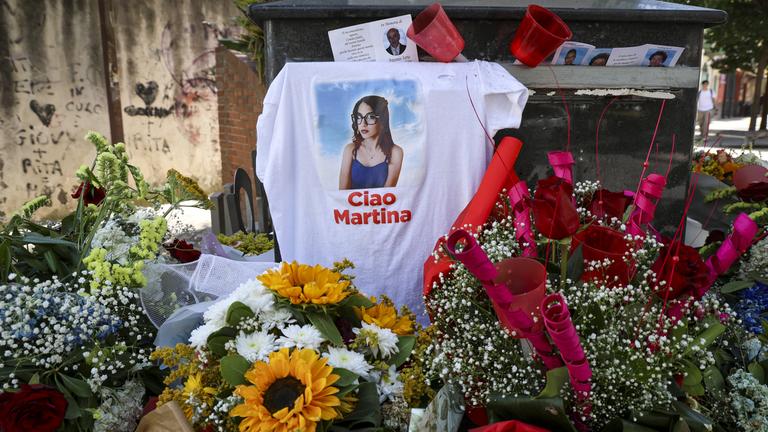 Ein T-Shirt, das über einem Grabstein hängt, zeigt ein Mädchen, am Boden mehrere Blumensträuße