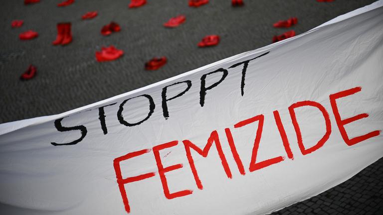Ein Banner mit der Aufschrift «Stoppt Femizide» hängt vor roten Schuhen.