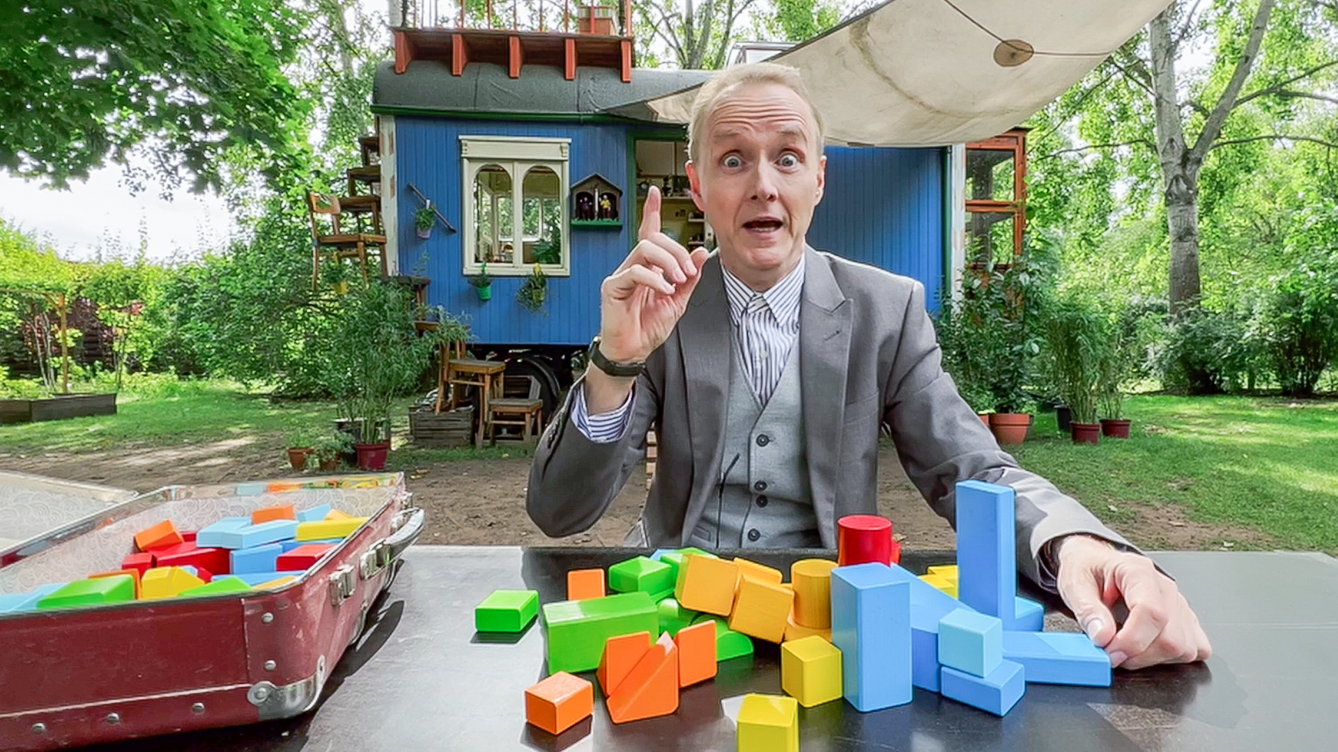 Kluthe sitzt an einem Tisch vor dem Bauwagen, auf dem viele bunte Bauklötze liegen