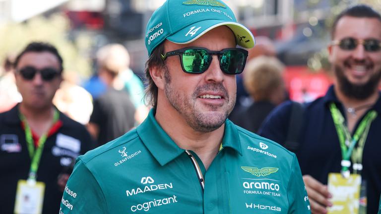 Fernando Alonso läuft mit Sonnenbrille, Kappe und grünem Aston Martin Shirt in Richtung Kamera