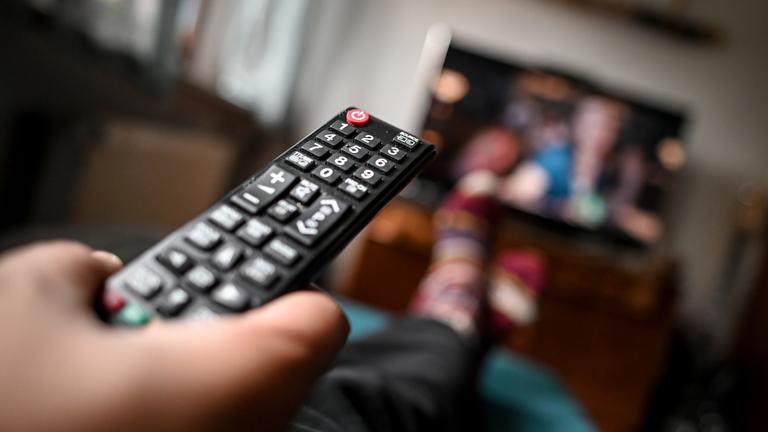 Eine Person sitzt mit Fernbedienung vor dem Fernseher.