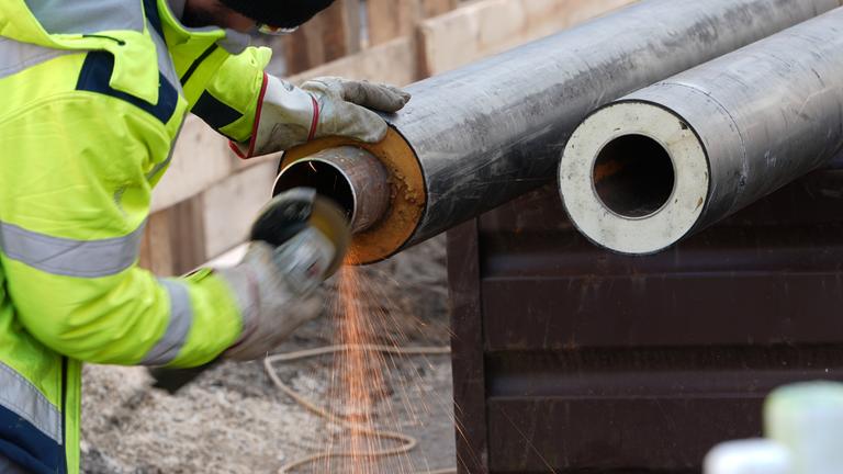 Symbolbild für Fernwärme: Arbeiter bereiten Rohre für Fernwärmeleitungen auf einer Baustelle vor