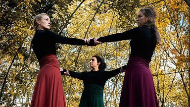 Drei Frauen halten sich im Wald an den Händen im Kreis.