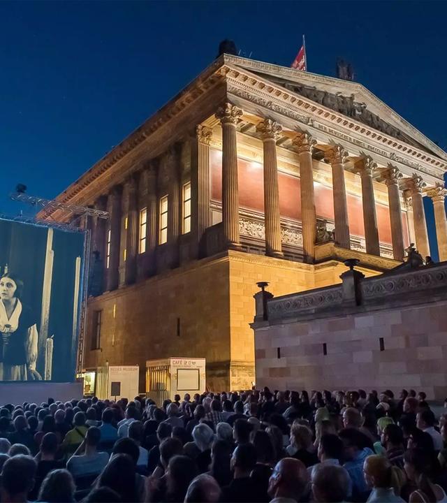 Man sieht ein historisches Gebäude, das aussieht wie ein griechischer Tempel, mit einer Kinoleinwand daneben, auf der ein Film vor Publikum gezeigt wird.