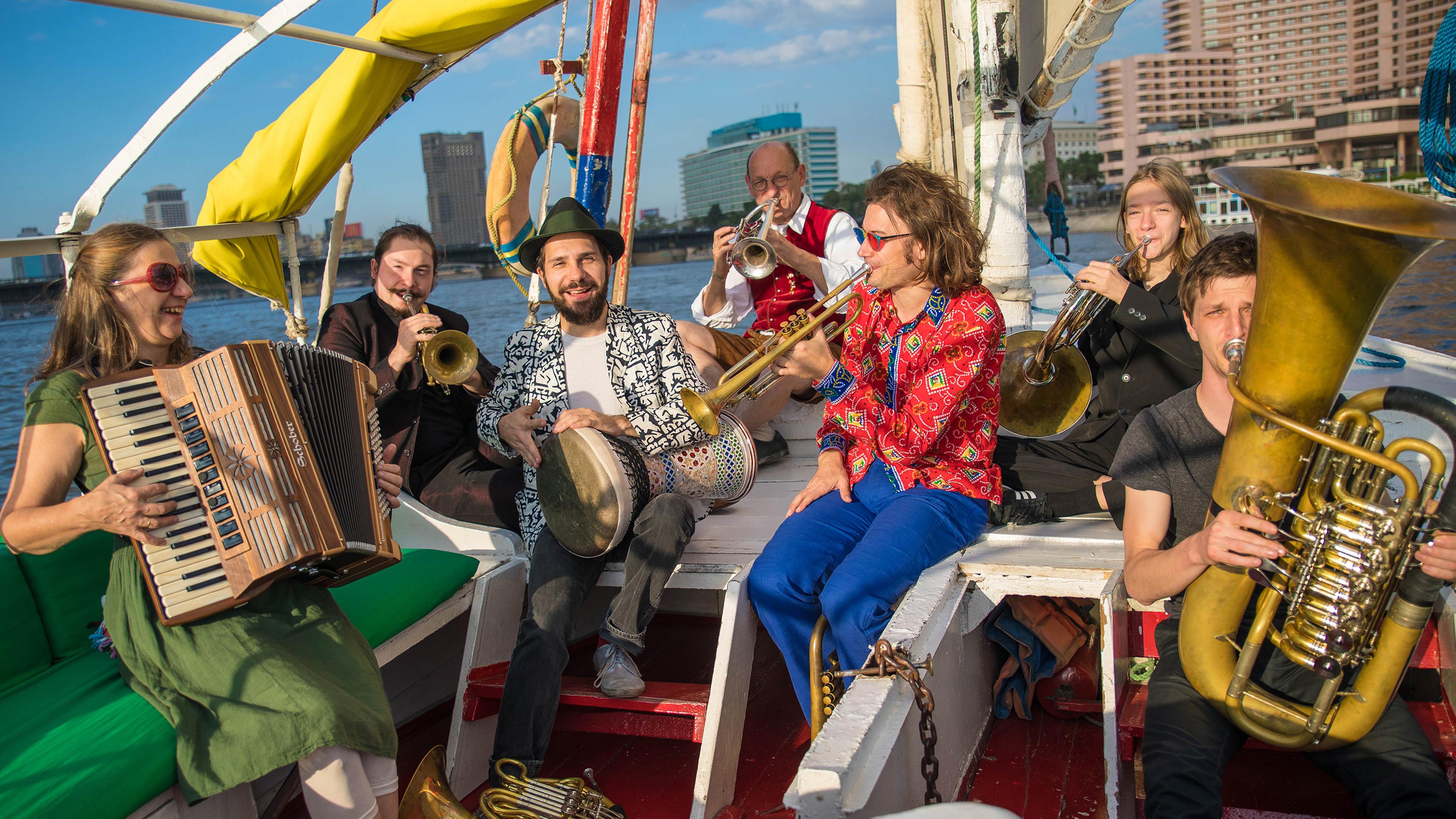 Menschen mit Musikinstrumenten sitzen auf einem Schiff.