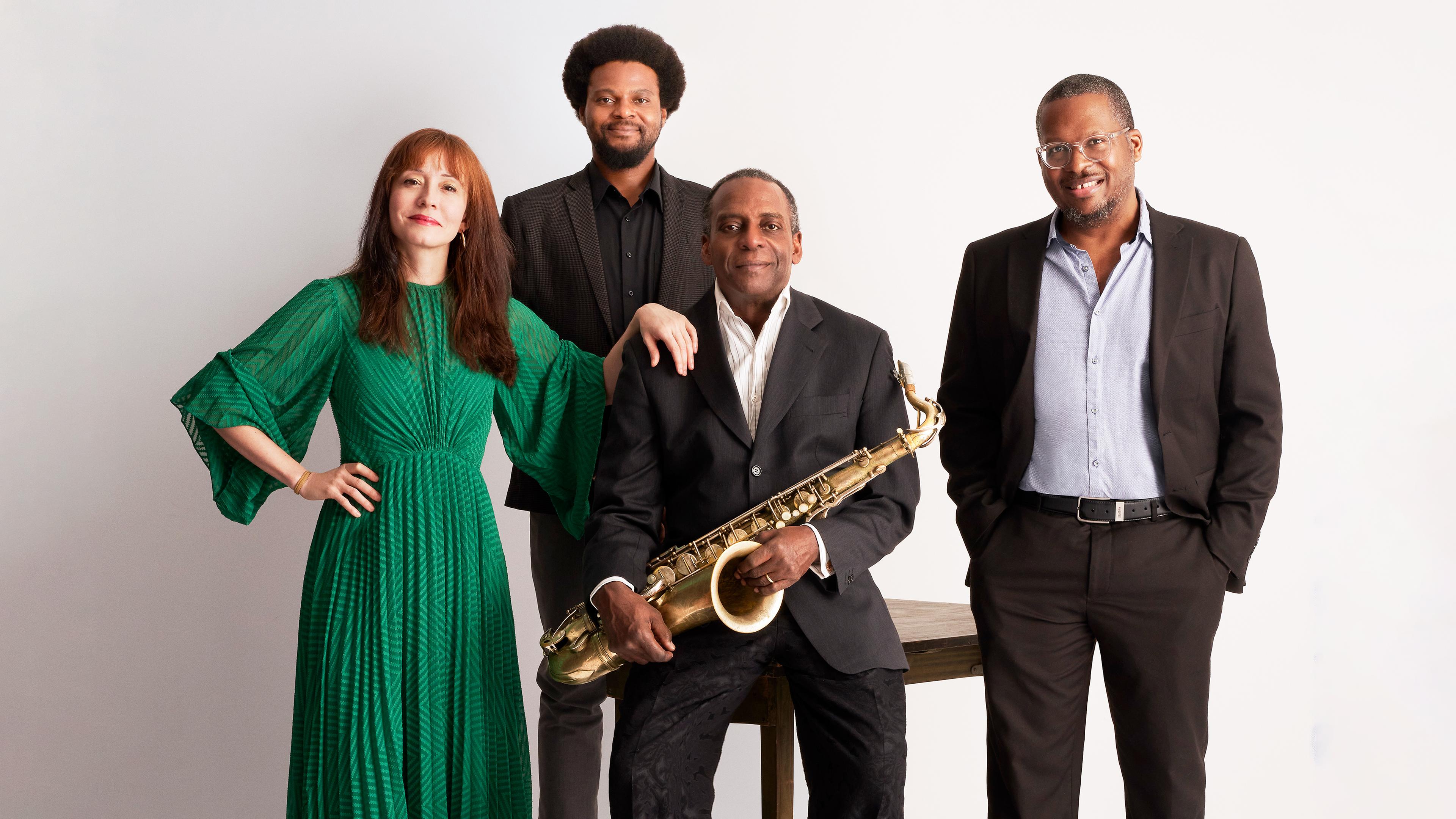 Eine Frau in grünem Kleid steht links von drei Männern in Anzug. Ein Mann hält ein Saxophon in seinen Händen.