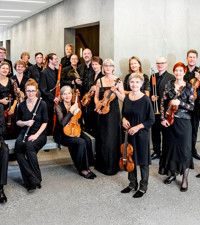 Die Mitglieder eines großen Streich-Orchesters haben sich für ein Gruppenfoto in einem modernen Vorraum versammelt.