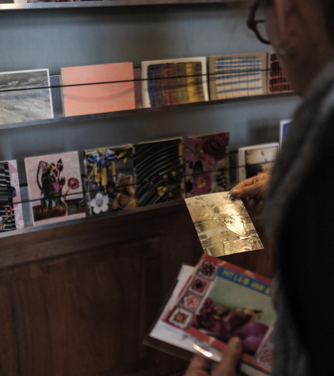 Ein Mensch schaut sich Postkarten an, die an einer Wand ausgestellt sind.