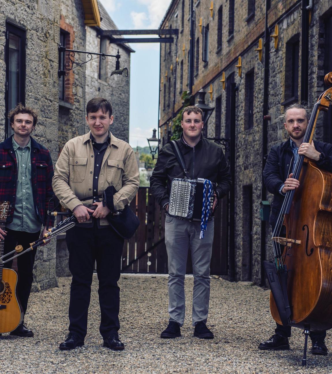 Vier Männer mit Musikinstrumenten stehen vor historischen Stein-Häusern.
