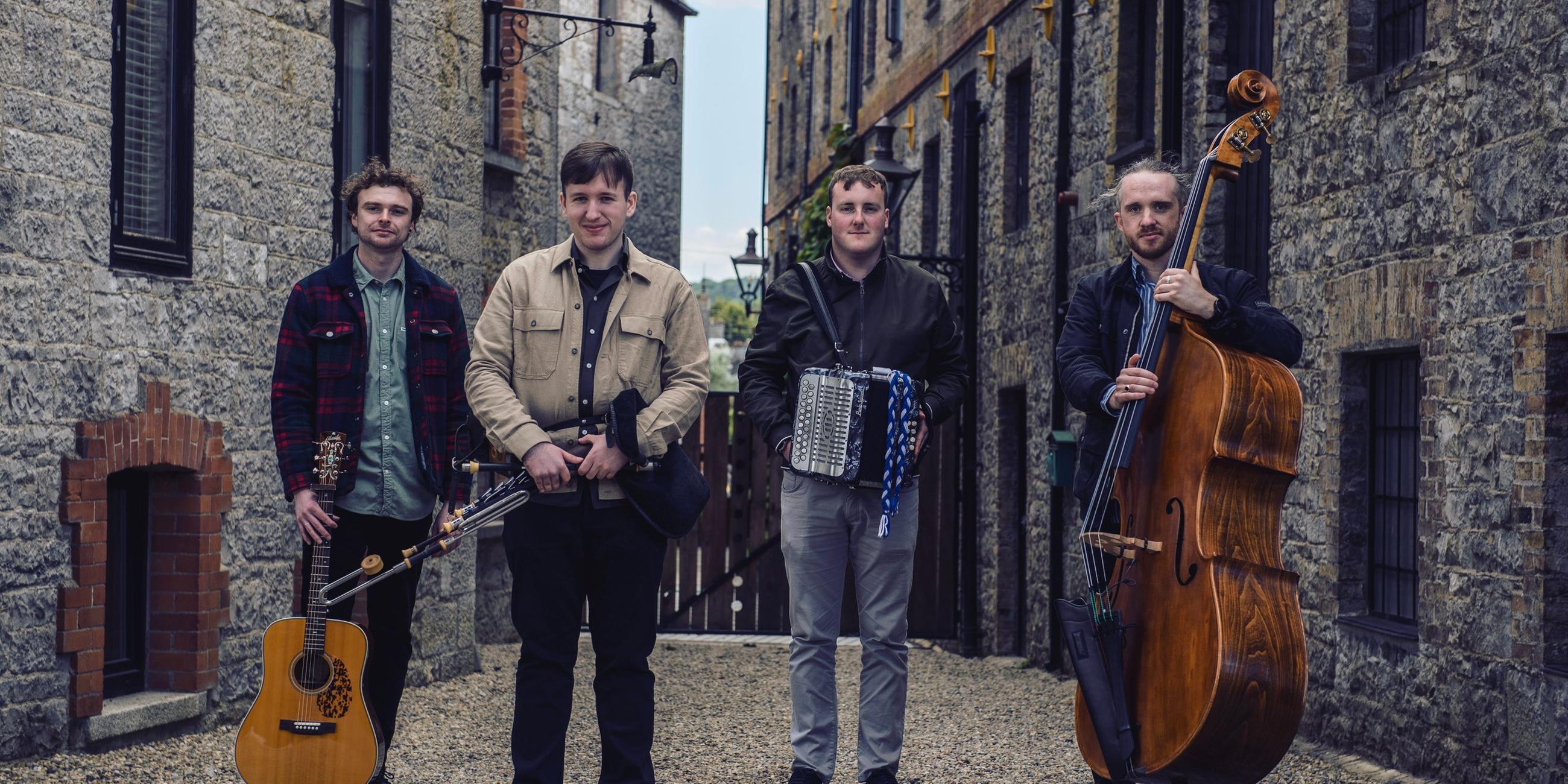 Vier Männer mit Musikinstrumenten stehen vor historischen Stein-Häusern.