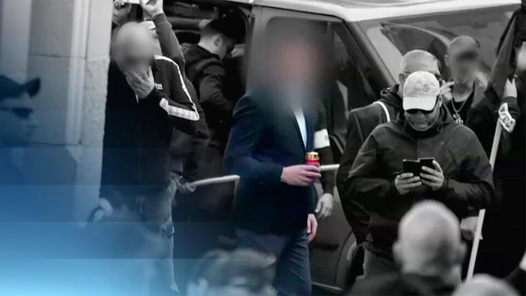 Mehrere dunkel gekleidete Männer stehen vor einem Auto