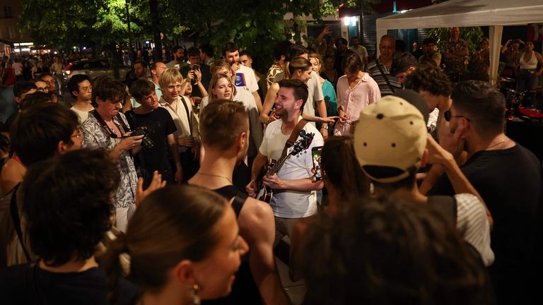 Musikbegeisterte hören einem Mann zu, der beim jährlichen französischen Straßenmusikfestival „Fête de la Musique“ Gitarre spielt.