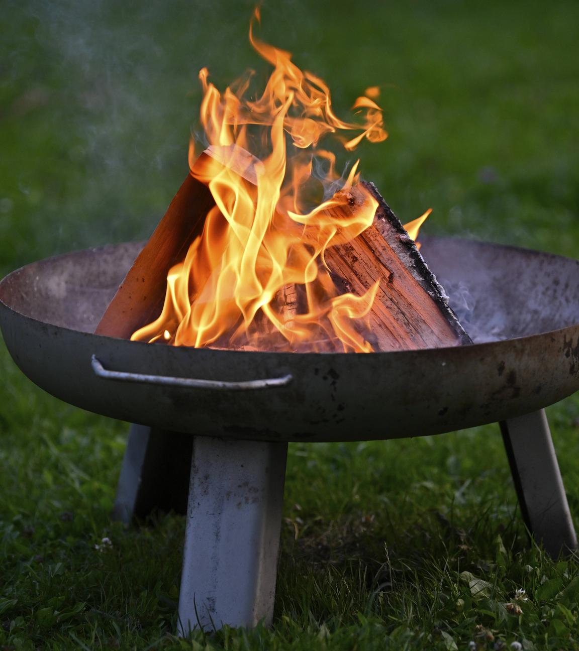 Eine brennende Feuerschale steht auf dem Rasen.