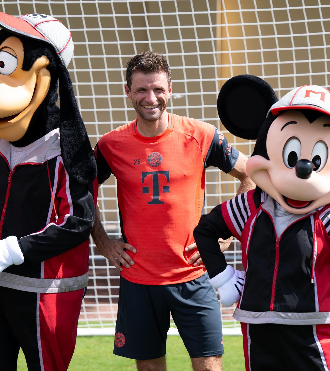 Thomas Müller steht nach dem Traning mit Goofy und Micky Maus für ein Foto zusammen.