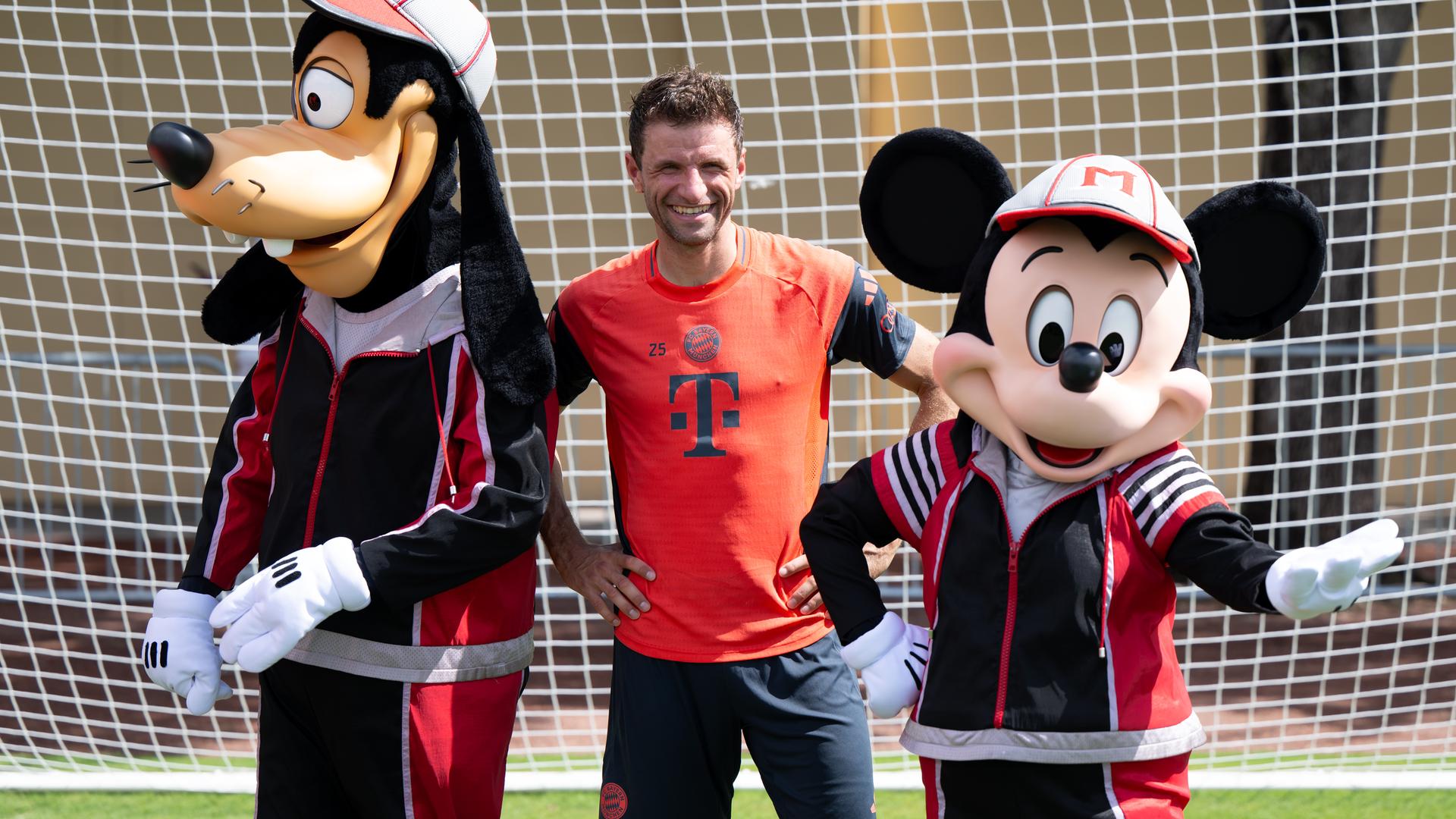 Thomas Müller steht nach dem Traning mit Goofy und Micky Maus für ein Foto zusammen.