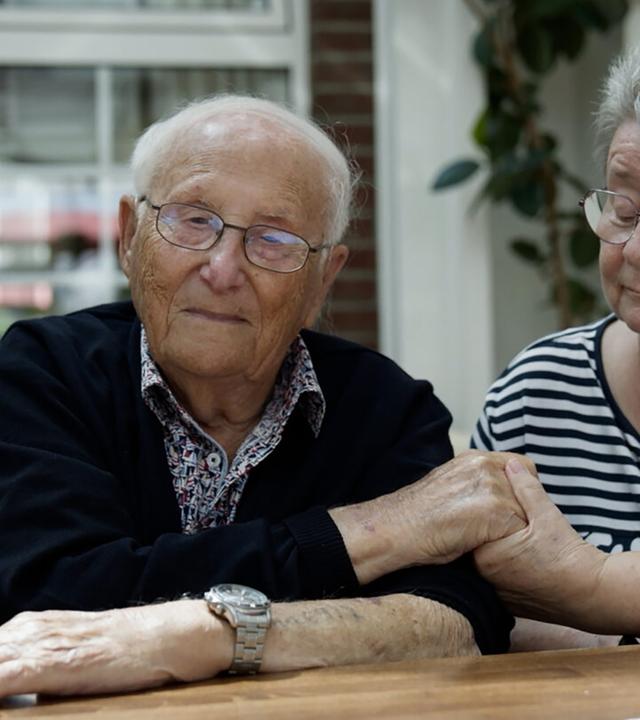 Ein älterer Mann und ein ältere Frau halten einander die Hand.