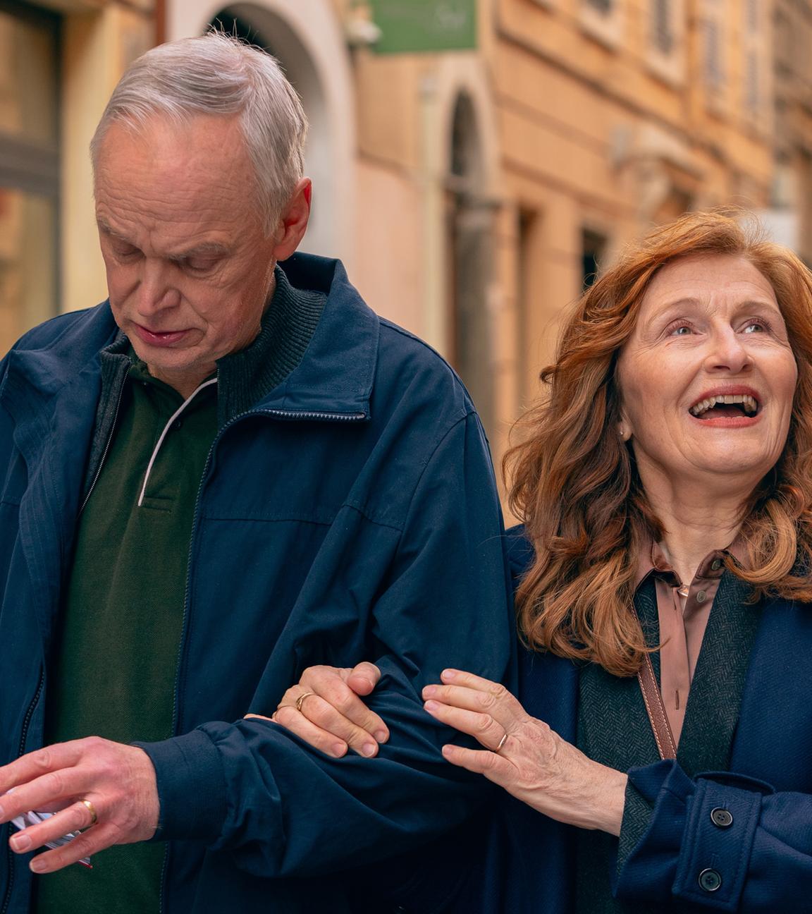 Ein älterer Mann und eine Frau laufen, an den Armen eingehakt, durch eine Stadt.