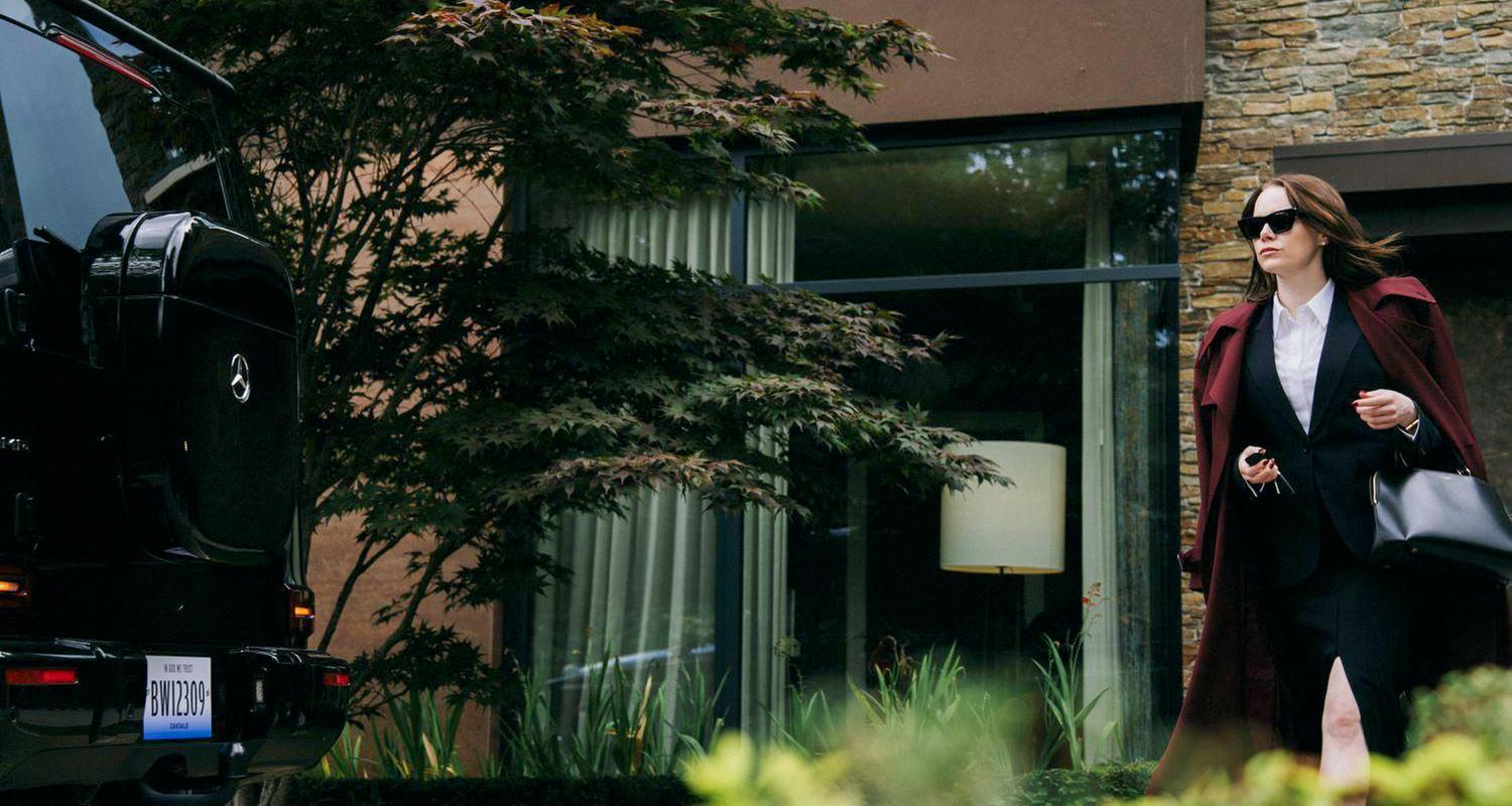 Eine Frau, die ein Businesskostüm und Sonnenbrille trägt, geht zu einem Auto.