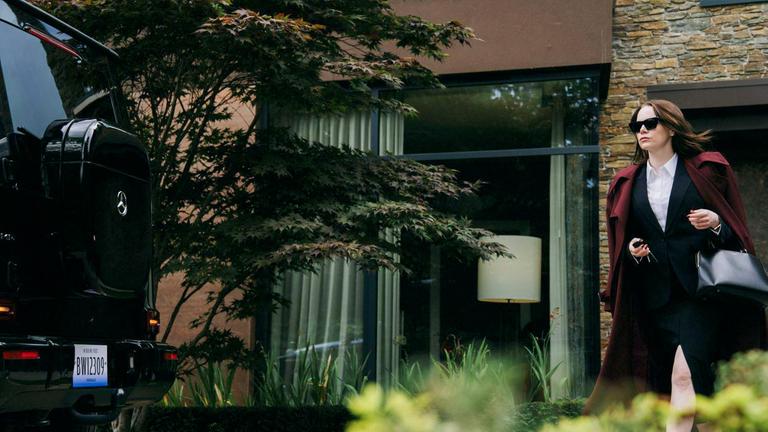 Eine Frau, die ein Businesskostüm und Sonnenbrille trägt, geht zu einem Auto.